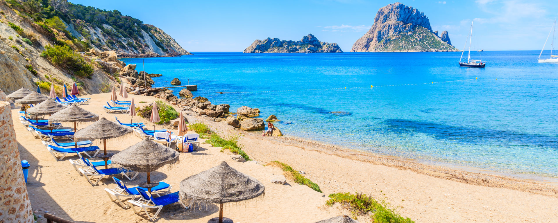 View of Cala d'Hort beach with sunbeds and umbrellas and beautiful azure blue sea water, Ibiza island, Spain