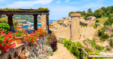 Flowers on coastal path in Tossa de Mar and view of castle with old town, Costa Brava, Spain